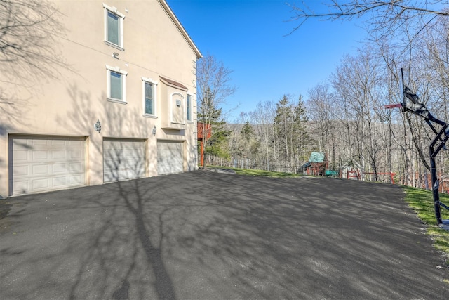 view of side of property featuring stucco siding, an attached garage, aphalt driveway, and a playground