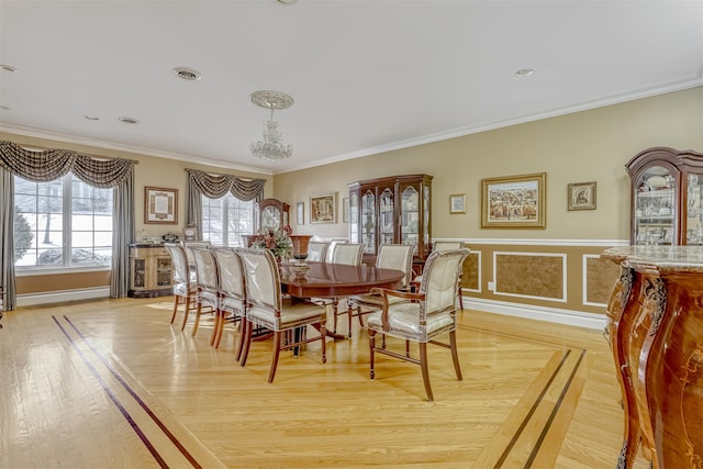 dining room featuring light wood-style floors, visible vents, ornamental molding, and wainscoting