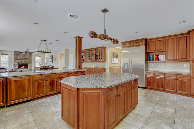 kitchen featuring stainless steel built in refrigerator, tasteful backsplash, visible vents, brown cabinets, and light stone countertops