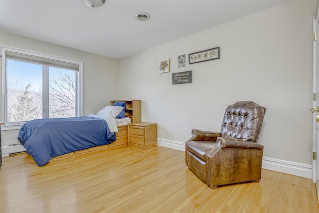 bedroom featuring a baseboard radiator, wood finished floors, visible vents, and baseboards