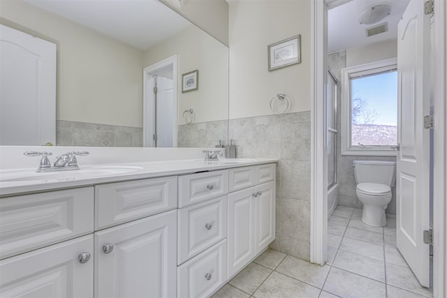 full bath with tile patterned flooring, double vanity, toilet, a sink, and tile walls