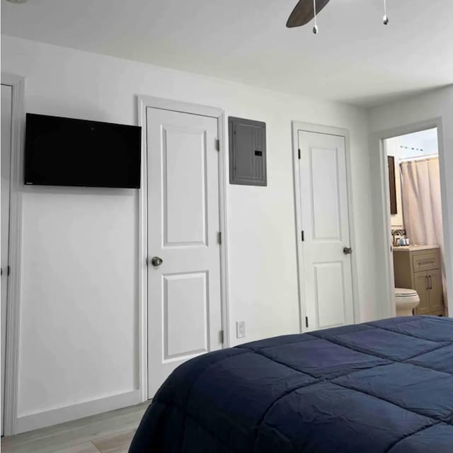 bedroom with light wood-type flooring, electric panel, baseboards, and ensuite bathroom