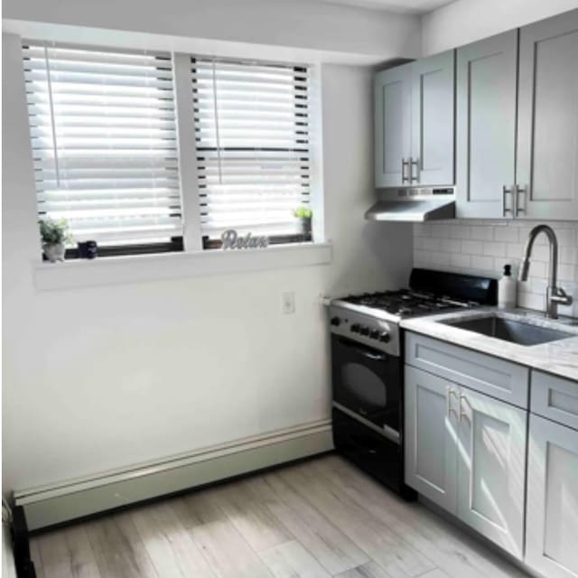 kitchen featuring range with gas stovetop, tasteful backsplash, a baseboard heating unit, a sink, and under cabinet range hood