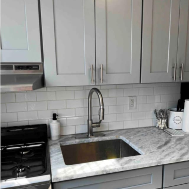 kitchen with gray cabinetry, a sink, range, and light stone countertops