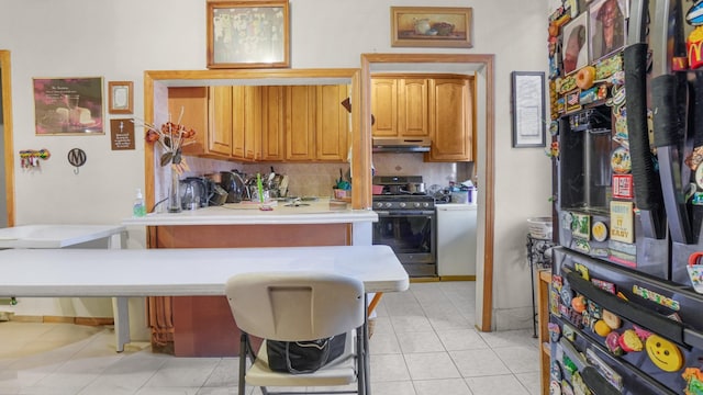 kitchen with light tile patterned flooring, under cabinet range hood, light countertops, decorative backsplash, and stainless steel gas stove