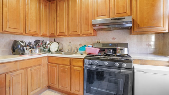 kitchen with under cabinet range hood, stainless steel gas range, light countertops, and a sink