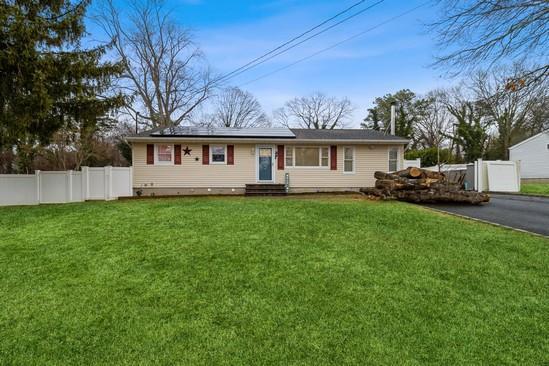 ranch-style home featuring entry steps, solar panels, a front yard, and fence