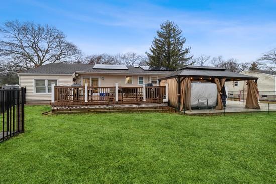 rear view of property featuring a gazebo, fence, a deck, a yard, and roof mounted solar panels