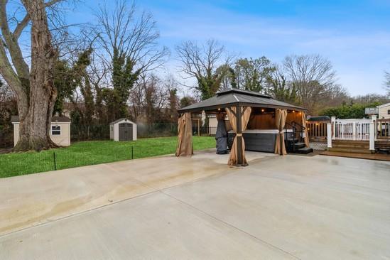 view of patio / terrace with concrete driveway, an outbuilding, a deck, a gazebo, and a shed