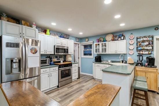 kitchen with light wood-style flooring, appliances with stainless steel finishes, white cabinetry, a sink, and a peninsula