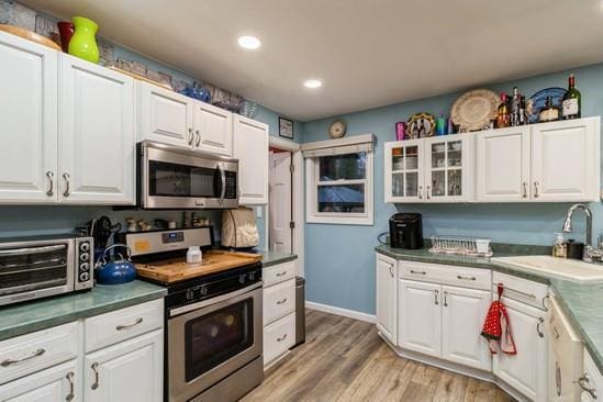 kitchen featuring a toaster, stainless steel appliances, light wood-style flooring, white cabinets, and a sink