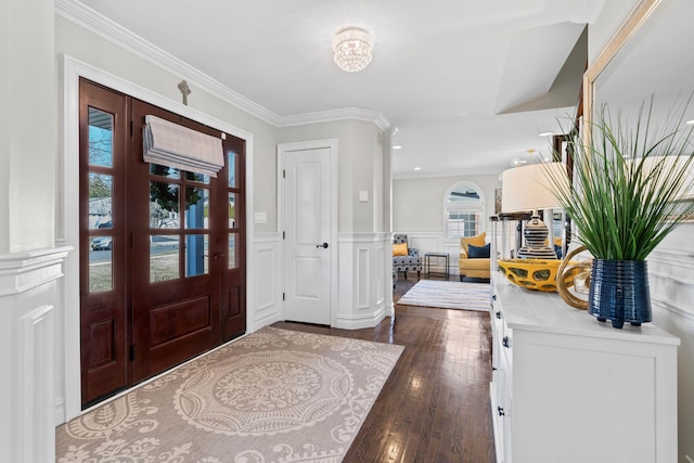 foyer entrance with ornamental molding, a decorative wall, dark wood-style flooring, and wainscoting