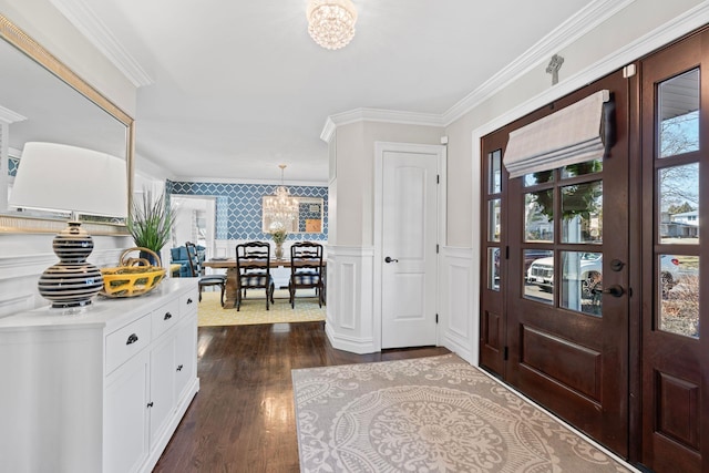 foyer entrance featuring a wainscoted wall, crown molding, dark wood-style floors, and an inviting chandelier