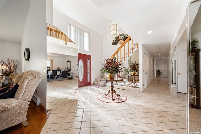 foyer entrance with a notable chandelier, light tile patterned floors, a towering ceiling, stairway, and baseboard heating