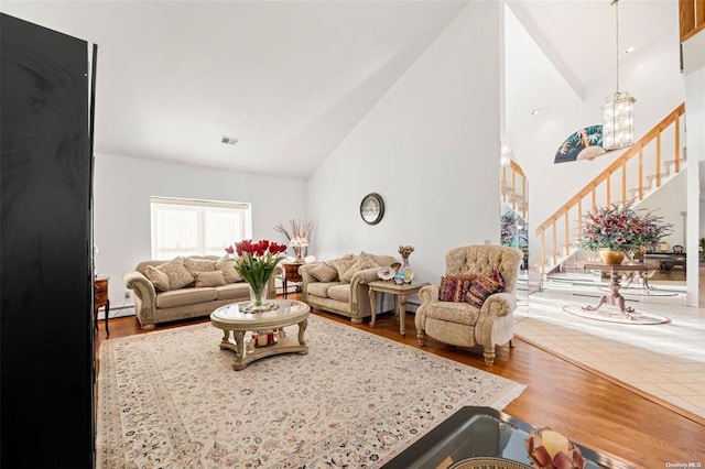 living room featuring high vaulted ceiling, wood finished floors, visible vents, stairs, and baseboard heating