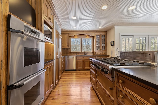 kitchen with appliances with stainless steel finishes, a healthy amount of sunlight, dark countertops, and brown cabinets