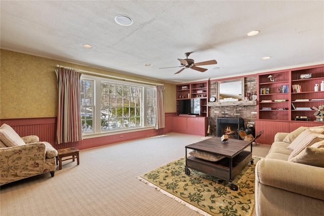 living room with wallpapered walls, a ceiling fan, a wainscoted wall, carpet floors, and a brick fireplace