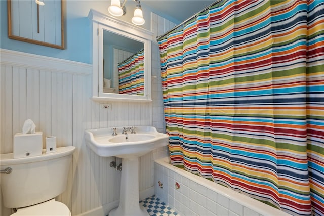 full bath featuring toilet, wainscoting, shower / tub combo with curtain, and a sink