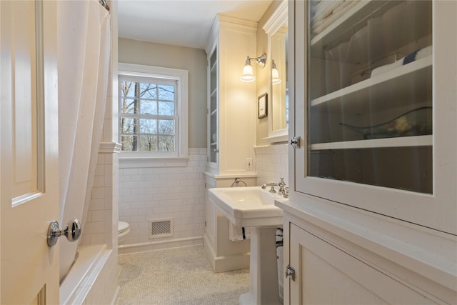 bathroom featuring visible vents, toilet, a shower with curtain, tile patterned floors, and tile walls