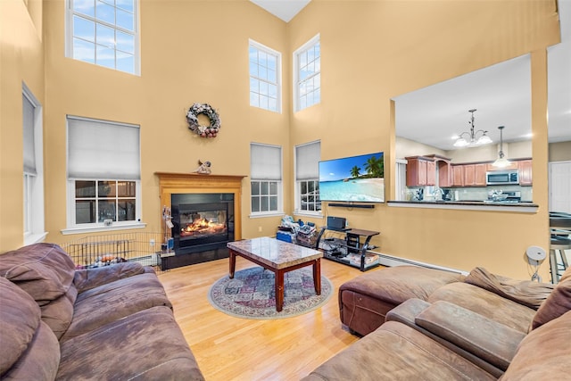 living area featuring light wood-type flooring, an inviting chandelier, a towering ceiling, and a glass covered fireplace