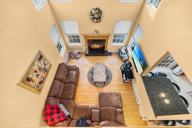 living area with a towering ceiling, wood finished floors, and a glass covered fireplace