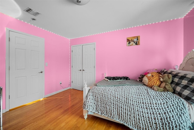 bedroom with a closet, wood finished floors, visible vents, and baseboards