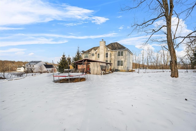 snow covered house featuring a trampoline and a chimney