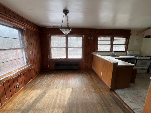 kitchen featuring radiator, light countertops, hanging light fixtures, wood walls, and white gas range oven