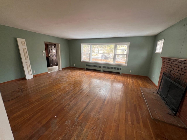 unfurnished living room featuring baseboards, dark wood-type flooring, a brick fireplace, and radiator