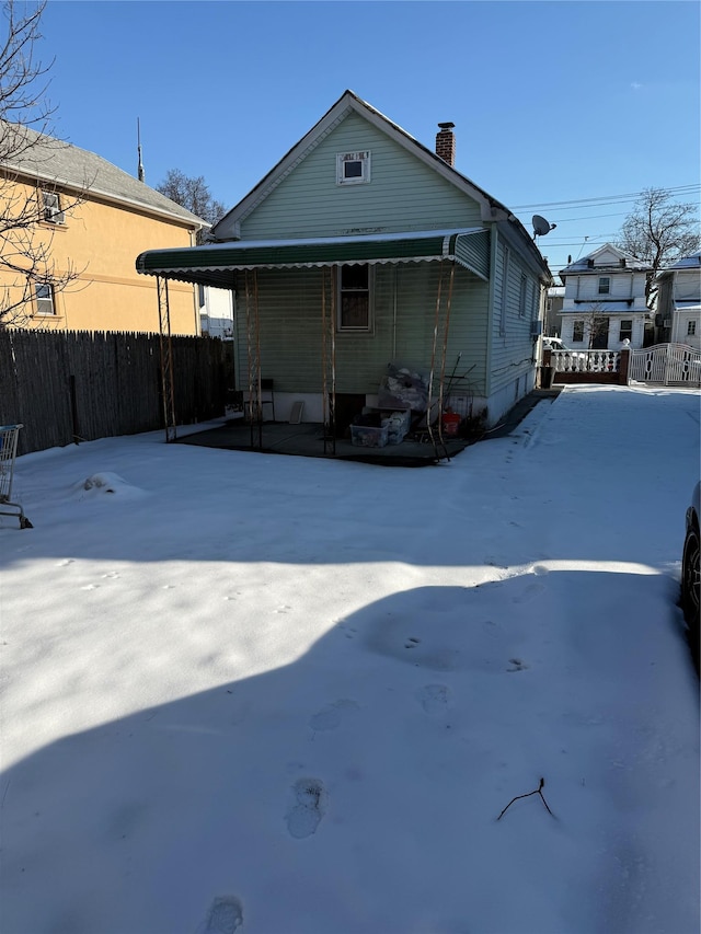 snow covered back of property featuring a chimney and fence