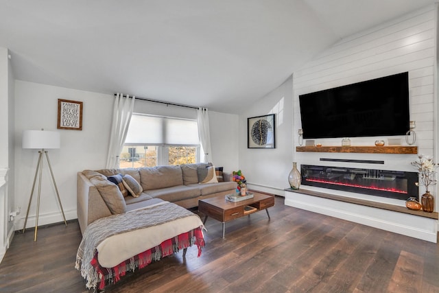 living room with dark wood-type flooring, a glass covered fireplace, and vaulted ceiling