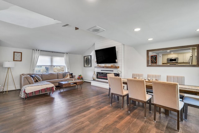 dining area featuring lofted ceiling, dark wood-style flooring, visible vents, and a glass covered fireplace