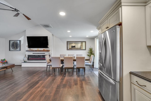 dining space featuring vaulted ceiling, dark wood-style flooring, a glass covered fireplace, and visible vents