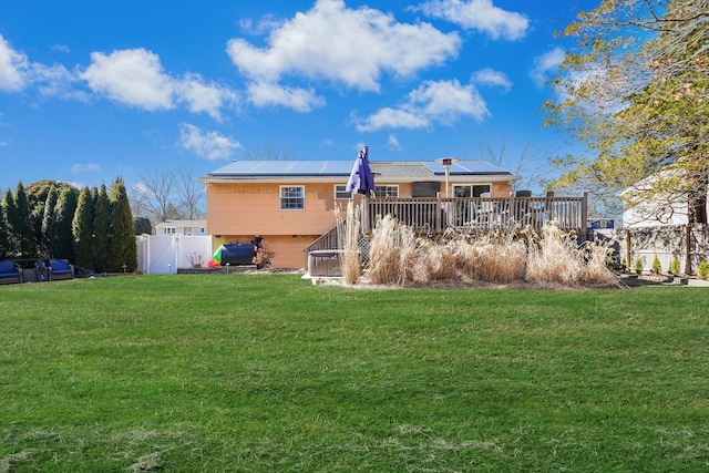 rear view of house featuring solar panels, a lawn, a wooden deck, and fence