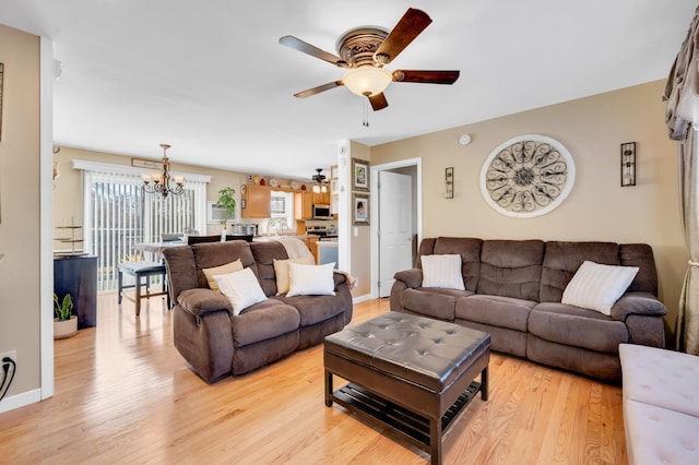 living room with baseboards, a healthy amount of sunlight, light wood finished floors, and ceiling fan with notable chandelier