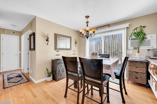 dining room with a wall unit AC, light wood finished floors, baseboards, and a notable chandelier