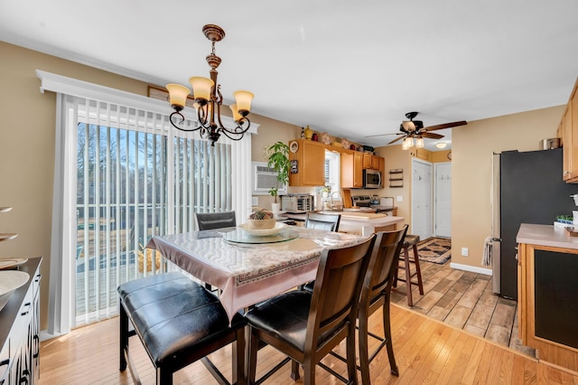 dining room with light wood-type flooring, a wall unit AC, baseboards, and ceiling fan with notable chandelier