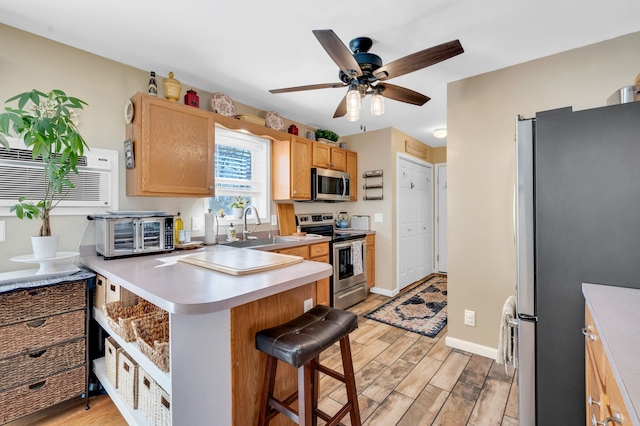 kitchen featuring a breakfast bar area, stainless steel appliances, a sink, light countertops, and light wood finished floors