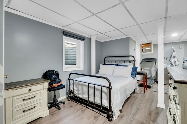 bedroom with light wood-type flooring, a paneled ceiling, and baseboards