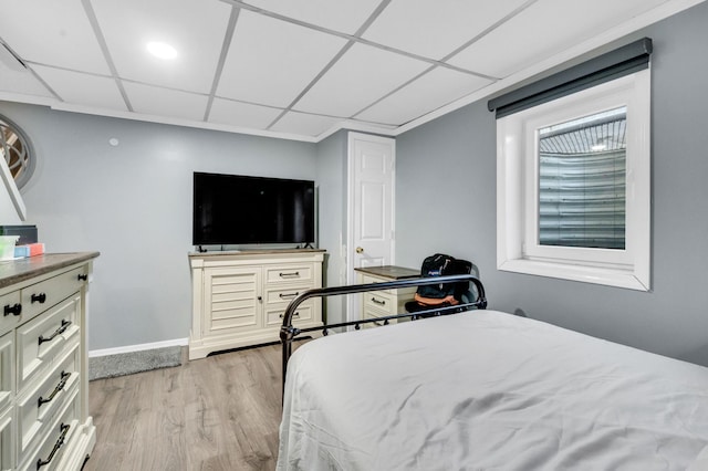 bedroom with a paneled ceiling, light wood-style flooring, and baseboards