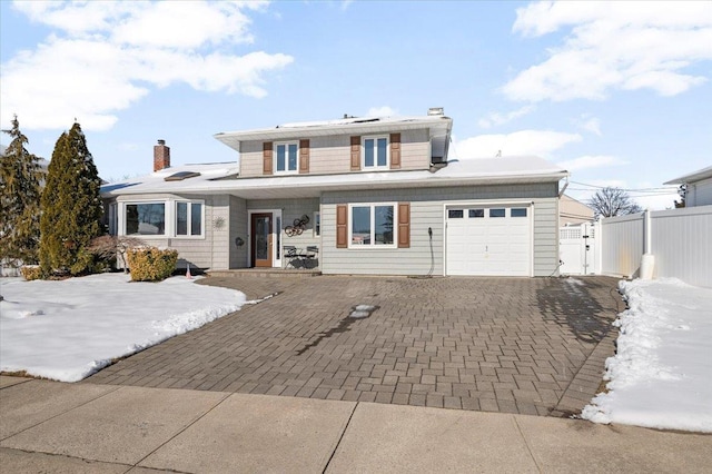 view of front of home with decorative driveway, a chimney, an attached garage, a gate, and fence