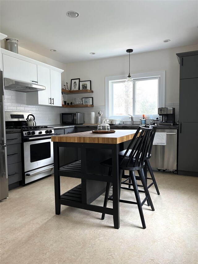 kitchen featuring tasteful backsplash, appliances with stainless steel finishes, light floors, decorative light fixtures, and under cabinet range hood