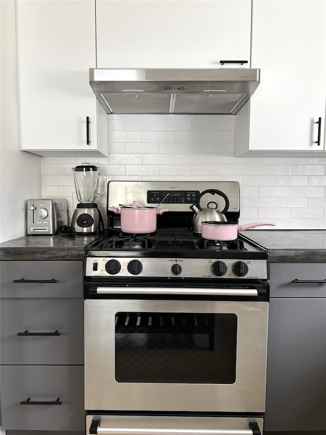 kitchen featuring stainless steel gas range, wall chimney range hood, white cabinetry, and backsplash