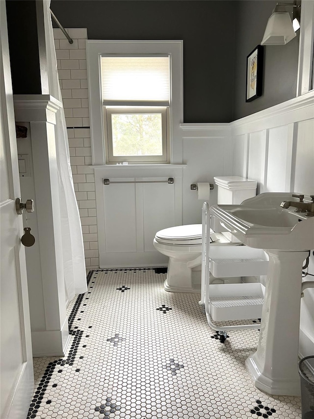 bathroom with toilet, a wainscoted wall, a shower with curtain, and a decorative wall