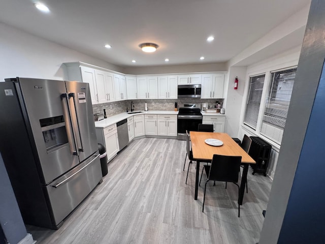 kitchen with light countertops, appliances with stainless steel finishes, light wood-style floors, white cabinets, and a sink