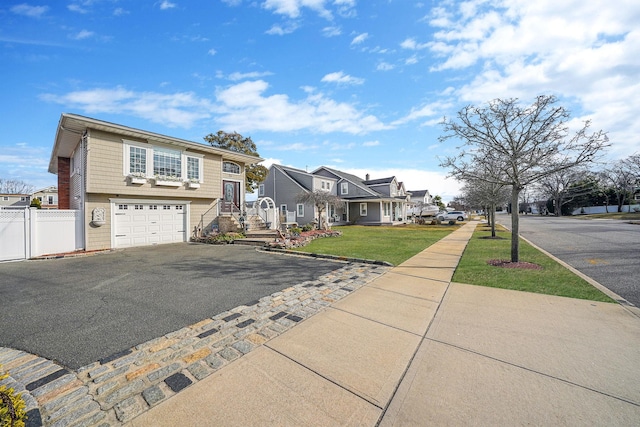 view of front of property featuring a garage, fence, driveway, a residential view, and a front lawn