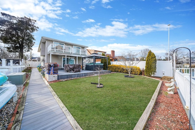 rear view of house with a fenced backyard, a balcony, a gazebo, a yard, and a hot tub