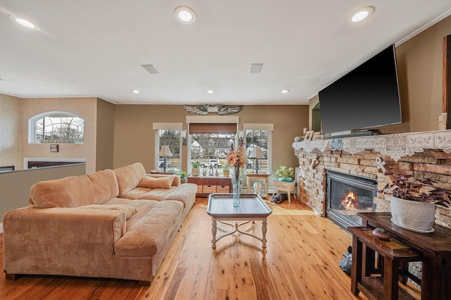 living area with recessed lighting, visible vents, a stone fireplace, and light wood finished floors