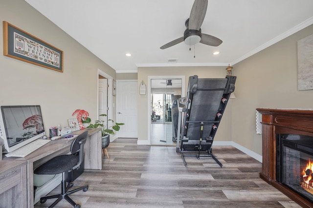 office space featuring a warm lit fireplace, baseboards, wood finished floors, and ornamental molding