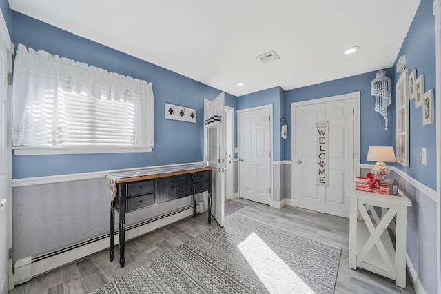 foyer entrance featuring a wainscoted wall, a baseboard radiator, wood finished floors, and visible vents